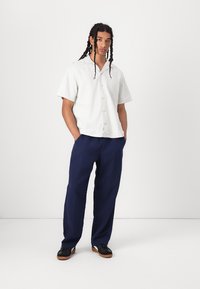 Chemise à manches courtes rayée vert clair avec des boutons, associée à un pantalon navy ample et des chaussures noires avec des semelles brunes.