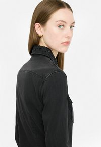 Giacca di jeans nera con colletto testurizzato arricchito da piccole perline nere. Il design include una tasca laterale e una vestibilità su misura.