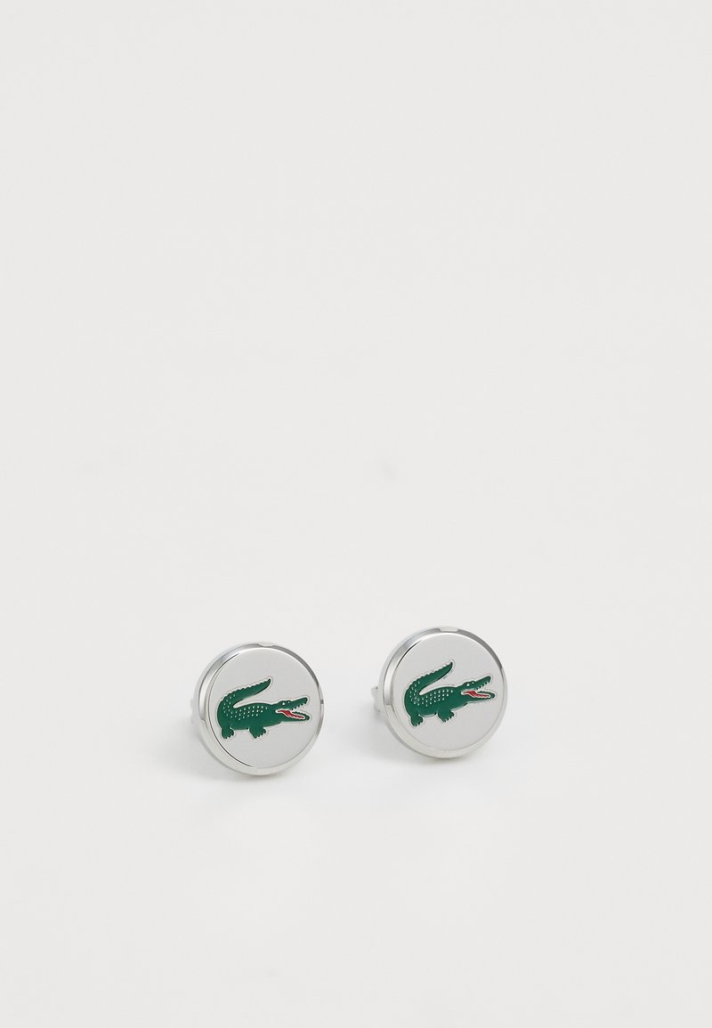 Manschetes de prata redondas com um logótipo de crocodilo verde com detalhes em vermelho, superfície polida e textura suave.
