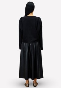 Zwarte trui met een relaxte pasvorm en lange mouwen, gecombineerd met een zwarte geplooide rok van nepleer, enkelhoog, met een gladde textuur.