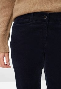 Marineblauwe ribfluweel broek heeft een geribbelde textuur, knoopsluiting en zijzakken. Aan de bovenkant is een beige gebreide trui zichtbaar.