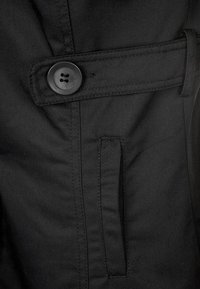 Czarna kurtka z tkaniny o gładkiej fakturze, z okrągłym czarnym guzikiem i wsuwaną kieszenią z przodu. Krój dopasowany.