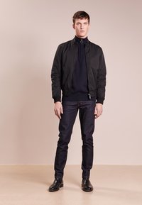 Schwarze Bomberjacke, marineblauem Pullover, dunklen Jeans, schwarze Chelsea-Stiefel; glatte Texturen, figurbetontes Design, lässiger Stil, minimale Akzente.