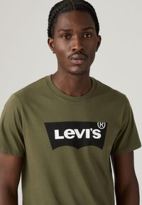 T-shirt de algodão verde-azeitona com um grande logótipo preto da Levi's com letras brancas, gola redonda, mangas curtas e textura suave.