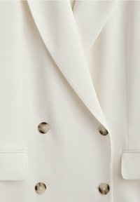 Blazer blanc croisé à larges revers, quatre boutons ronds beiges et poches à rabat de chaque côté.