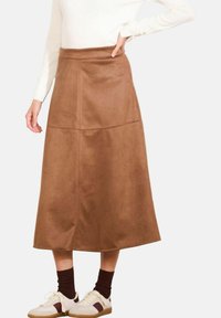 Brown faux suede midi skirt with a smooth texture, A-line shape, side seam pockets, and stitched panels. Paired with white sneakers and burgundy socks.