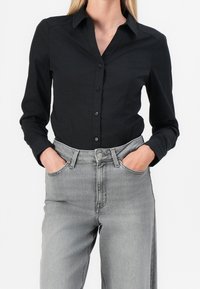 Camicia nera a maniche lunghe con chiusura a bottoni e colletto a punta, abbinata a jeans in denim grigio chiaro a vita alta con tasche laterali.