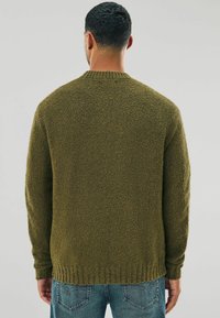 Textured olive green sweater with a ribbed neckline and cuffs, featuring a loose fit and long sleeves, worn over light blue jeans.