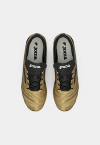 Scarpe sportive dorate con tomaia testurizzata, lacci neri e logo. Presentano una suola imbottita e una fodera interna grigia in contrasto.