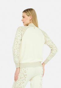 Maglione crema con maniche a stampa leopardata chiara, polsini e orlo a coste, dettaglio in oro sul collo posteriore, realizzato in morbido materiale a maglia.