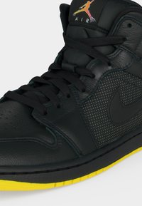 Μαύρο sneaker ψηλού τύπου με μαύρα κορδόνια, διάτρητη πλαϊνή επιφάνεια, κίτρινη σόλα και πολύχρωμο λογότυπο Jumpman με κείμενο "AIR" στη γλώσσα.