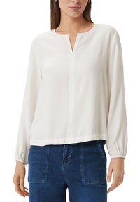 White long-sleeve blouse with a round neckline and subtle front placket. Soft fabric with a slightly structured fit. Paired with blue denim.
