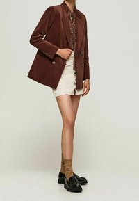 Hnědý kordový blejzr s vykrojenými klopy, na dva knoflíky, kombinovaný se vzorovanou košilí, denimovou sukní, ponožkami po kolena a masivními černými botami.