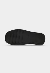 Semelle en caoutchouc noir d'une chaussure sans lacets avec des bandes de grip horizontales et le logo "Calvin Klein" embossé près du milieu.