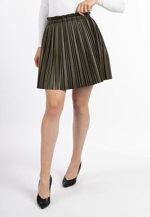 Olijfgroene geplooide rok van faux leer met een elastische tailleband. Gecombineerd met zwarte hoge hakken.