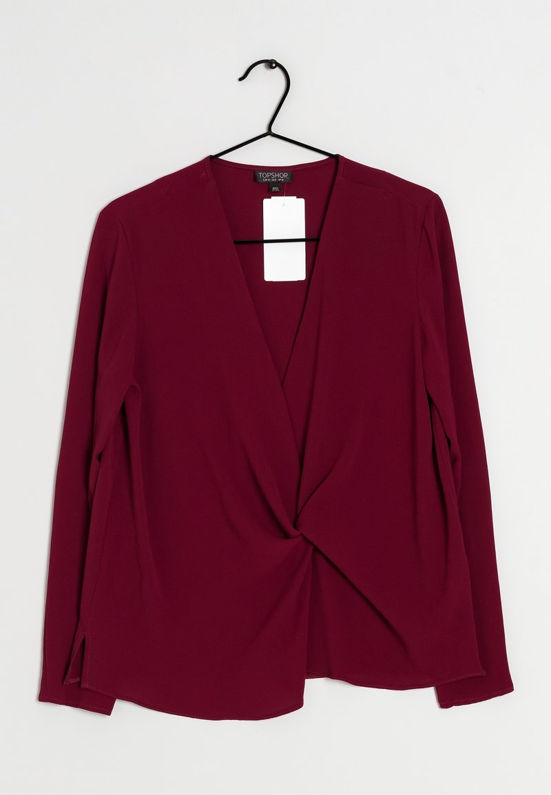 Top a maniche lunghe bordeaux con design avvolgente, dotato di scollo a V e spacchi laterali. Realizzato in un tessuto liscio, appeso a un gancio nero.
