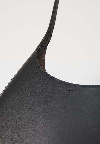 Fekete bőr kézitáska sima felülettel, kerek nyílással és vékony pánttal. Finom varrási részlet a szélein.