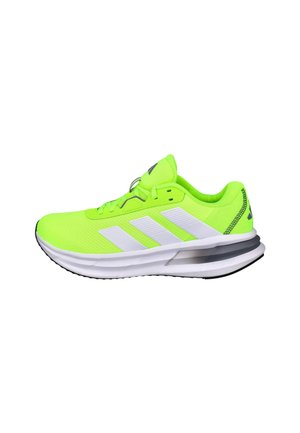 Zapatilla deportiva verde neón con diseño de tres rayas blancas, parte superior de malla, cuello acolchado y suela negra con un elemento de amortiguación visible.
