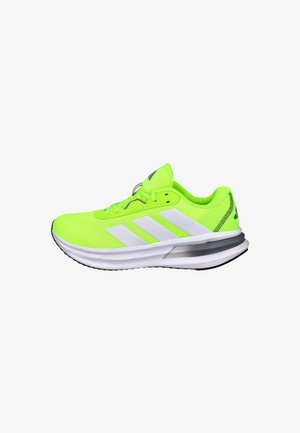Zapatilla deportiva verde neón con diseño de tres rayas blancas, parte superior de malla, cuello acolchado y suela negra con un elemento de amortiguación visible.