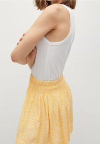 Débardeur blanc avec un décolleté arrondi et une jupe à motifs floraux jaunis avec une taille smockée, présentant de petites fleurs dispersées.
