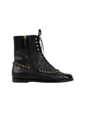 Bottine en cuir noir avec fermeture éclair latérale, œillets dorés, détail chaîne et bout brillant noir.