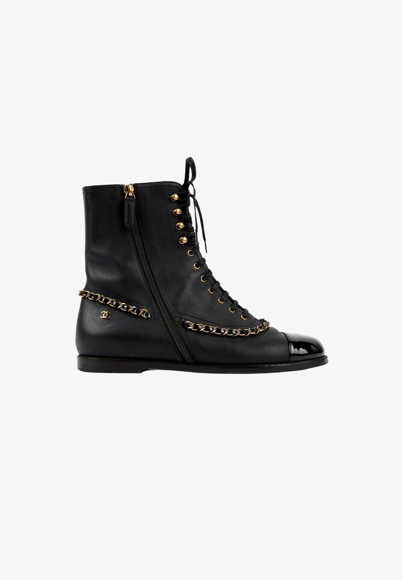 Bottine en cuir noir avec fermeture éclair latérale, œillets dorés, détail chaîne et bout brillant noir.