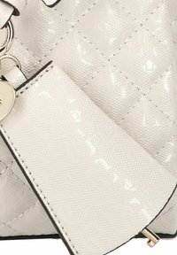 Witte faux lederen tas met een doorgestikt patroon, subtiele logo's, gestikte details en een goudkleurig metalen label.