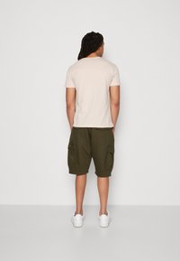Kort beige t-shirt og mørkegrønne cargo shorts med sidelommer og synlige sømme, parret med hvide sneakers.