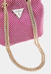 Borsa a tracolla rosa coperta di piccole borchie luccicanti. Presenta un logo triangolare argentato e catene intrecciate dorate. Superficie texturizzata.