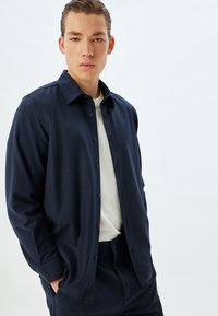 Navyblauw button-up shirt gemaakt van een gladde stof, met een klassieke kraag, voor knopen en een relaxte pasvorm. Draagt over een wit t-shirt.