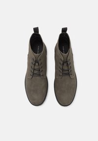 Botas de tobillo de ante verde oliva con cintas negras, punta redondeada y una lengüeta en el talón. Parte superior texturizada y suela contrastante.