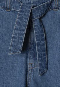 Denim audums vidēji zilos toņos ar jostu viduklī. Ievērojamas šuves un mīksta tekstūra, izceļot jostu cilpas un apdari.