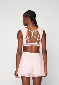 Lichtroze sportieve crop top met een mesh achterkant, voorzien van gekruiste bandjes. Gepaard met een bijpassende doorzichtige rok.
