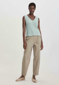 Licht mintgroene ribgebreide tanktop met een V-hals, gecombineerd met beige hoge taille broeken en lichtbruine instappers.