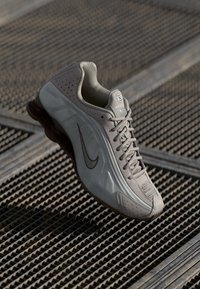 Baskets de sport gris clair avec une tige texturée, des perforations pour la ventilation, des accents marron et une semelle épaisse et rembourrée.