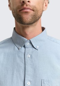 Lichtblauw overhemd met knopen, gemaakt van zacht materiaal, met een klassieke kraag en een borstzak met een klein logodetail.