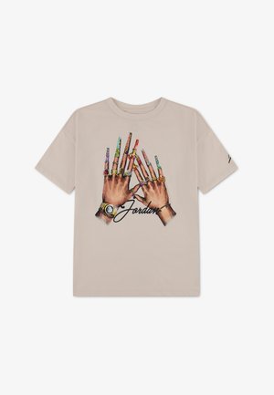 T-shirt beige avec un graphique de deux mains portant des bagues, des montres et de longs ongles décorés, ainsi que le mot "Jordan" en écriture manuscrite en dessous.