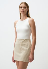 Witte geribde tanktop gecombineerd met een beige minirok met fijne strepen. De stof is soepel met verticale witte strepen en een getailleerd silhouet.