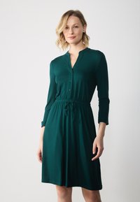 Vihreä, puolipitkä mekko kevyestä kankaasta, jossa on napitettava etuosa ja säädettävä naruvyötärö. Pitkät hihat, joissa on hihansuut.