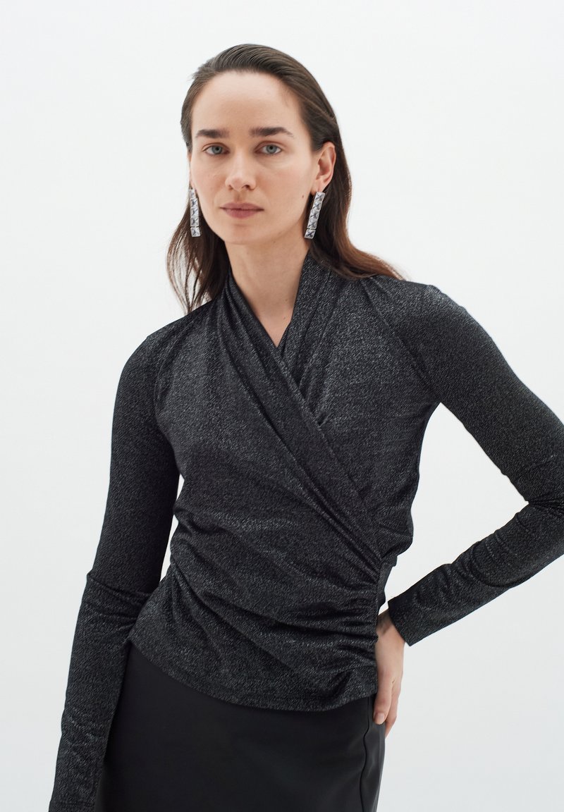 Top lungo a maniche lunghe nero, textured, con design avvolgente e dettagli arricciati in vita, caratterizzato da un leggero effetto lucido.