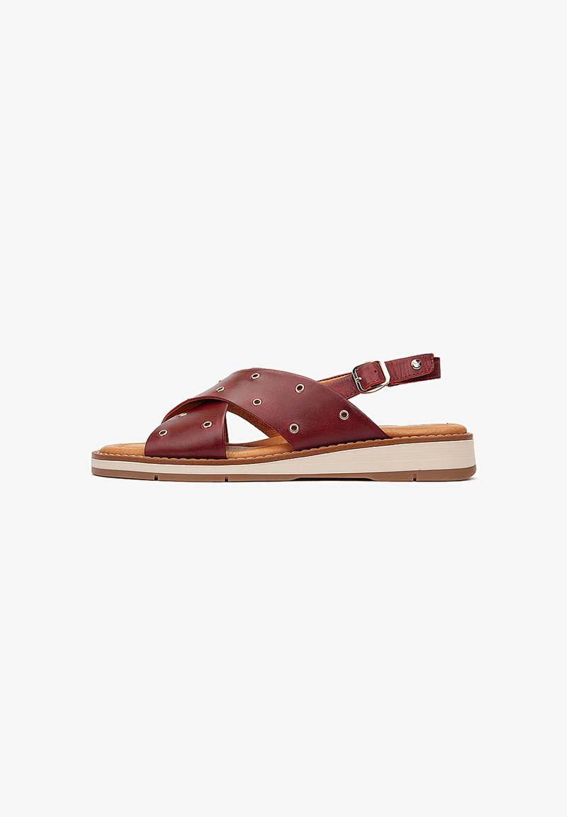 Sandale en cuir bordeaux avec des brides entrecroisées, des découpes circulaires, une sangle de cheville réglable et une semelle dégradée blanche.