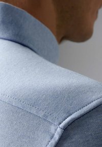 Lichtblauwe shirt met een gestructureerde stof. Close-up van de kraag, met details van de stiksels en een soepele overgang van de stof.