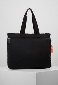 Sac fourre-tout en tissu noir avec deux poignées courtes, fermeture éclair sur le dessus et une poche extérieure. Comprend une étiquette rouge attachée au curseur de la fermeture éclair.