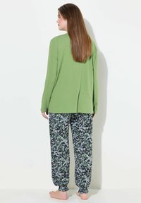 Top de manga larga verde combinado con pantalones de pijama de patrón floral en blanco y negro. Los pantalones tienen puños elásticos, ofreciendo un ajuste relajado.