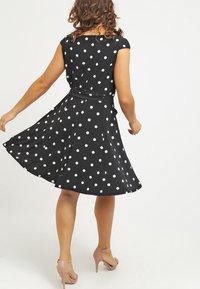 Musta pilkullinen mekko lyhyillä hihoilla, vyötäröltä kireä ja levenevä helma. Sileä kangas, polvipituinen helma. Yhdistetty vaaleanpunaisiin korkokenkiin.