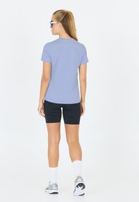 Maglietta sportiva azzurro chiaro a maniche corte abbinata a pantaloni ciclistici neri e calze bianche. Il modello indossa occhiali da sole e sneakers sportive.