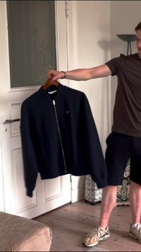 Dunkelblaues Zip-Hoodie aus weichem Stoff, mit Rundhalsausschnitt, gerippten Bündchen und kleinem Logo auf der Brust, auf einem Holzkleiderbügel aufgehängt.