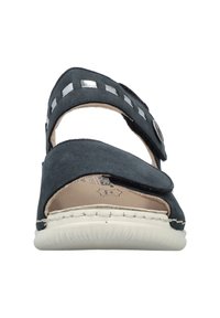 Sandal en daim noir avec une sangle ajustable présentant un accent métallique, une semelle intérieure texturée et une semelle en caoutchouc blanc. Design à bout ouvert.