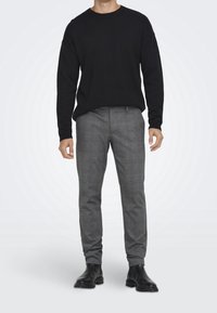 Zwarte gebreide trui, grijs geruite broek met een subtiele blauwe lijn, aansluitend ontwerp, gecombineerd met zwarte enkellaarsjes.