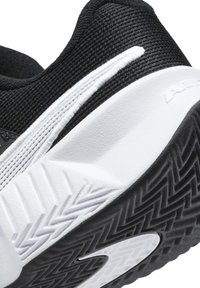 Scarpa sportiva nera con tomaia traforata, dettagli bianchi e suola in gomma con motivo a spina di pesce per aderenza e supporto.